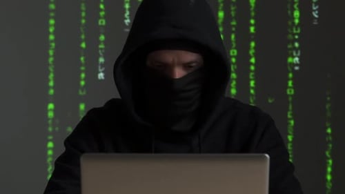 Hooded Hacker Typing on Laptop with Matrix Background