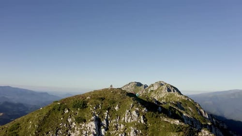 Hiker on Mountain Summit With Tents in Distance
