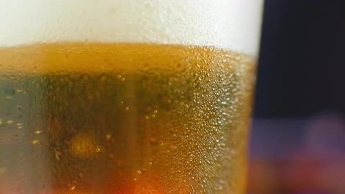 Close-up Slow Motion: Cold Beer in a Glass Large Drops and Bubbles in the Beer.