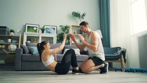 Jeune homme et femme faisant des situps et tapant des mains s'entraînant à la maison