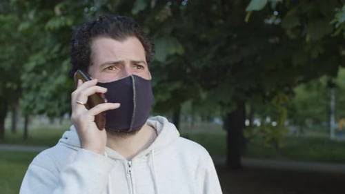 Zeitlupe eines gutaussehenden Mannes in Covid19-Gesichtsmaske, der auf jemanden im Park wartet
