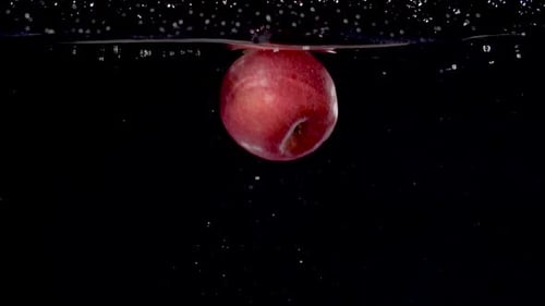 Bunter roter Apfel wird in Zeitlupe ins Wasser geworfen.