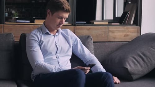 Young Man Using Smartphone on Gray Couch