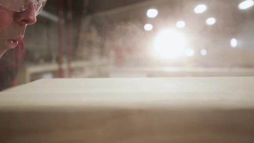 Man Blowing Dust Off Wood in Workshop Close-Up