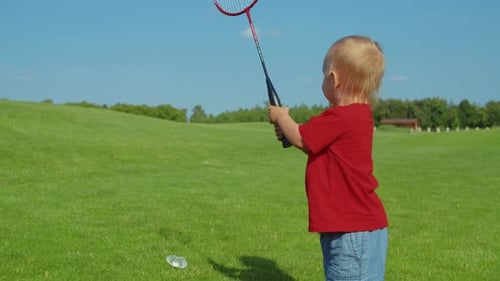 Toddler Holding Badminton Racket in Green Field. Cute Boy Jumping in Air