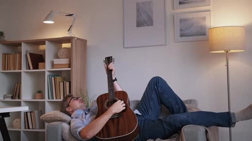 Adult Man Plays Guitar Lying on Sofa