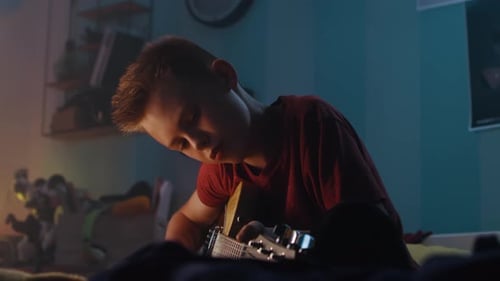 Teenager Practicing Guitar in Dimly Lit Bedroom