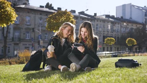Two Young Women Looking at Tablet in City Park