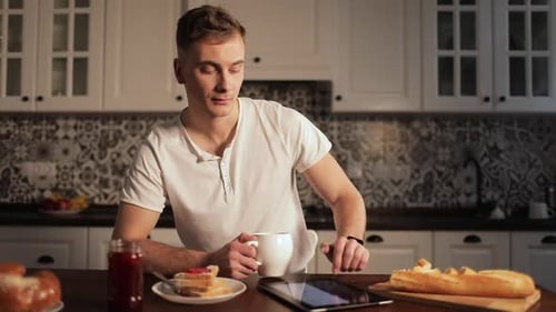 Man Drinks Coffee and Uses Tablet at Breakfast