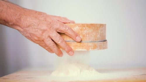 Hand Sifting Flour over Pile on Wood Table