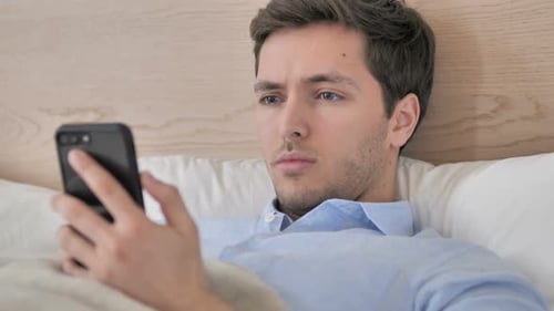 Man Using Smartphone While Lying in Bed