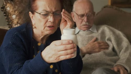 Senior Woman Reads Medicine Label for Elderly Man