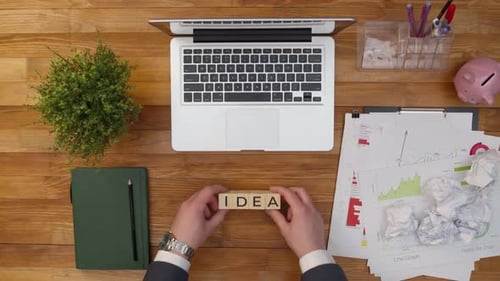 Word Idea of Wooden Cubes is Folded with Hands on a Table in the Office