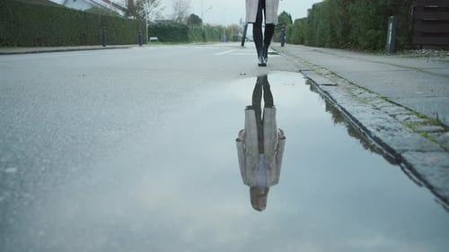 Woman Walks Toward Camera Reflected in Puddle