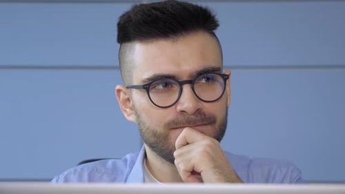 A Young Thoughtful Man Thinks About A Problem Works On A Startup Project Online On A Computer