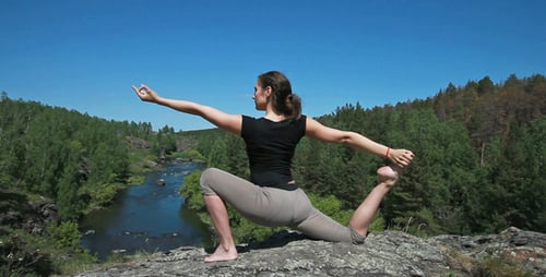Woman Practicing Yoga on Rocky Riverbank in Nature
