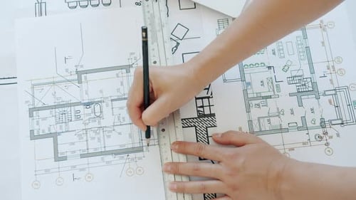 Blick von oben auf eine Architektin in der Hand, die einen Bauplan zeichnet, konzentriert auf den Bauplan