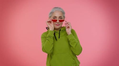 Senior Woman Posing With Red Sunglasses on Pink
