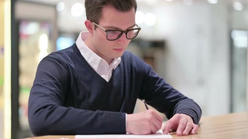 Young Man Concentrates Writing with Pen on Paper