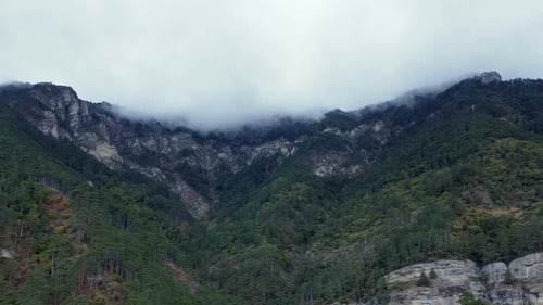 Aerial footage of rocky green forests with a misting up high mountains in the background