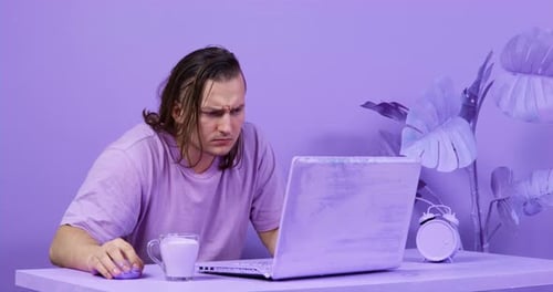 Serious Student Does Coursework on Laptop at Table in Room