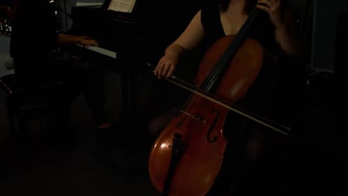 Woman Plays Cello With Pianist in Dim Lighting