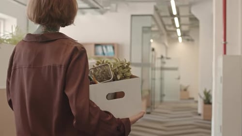 New Female Office Worker Walking Along Corridor Carrying Box of Stuff