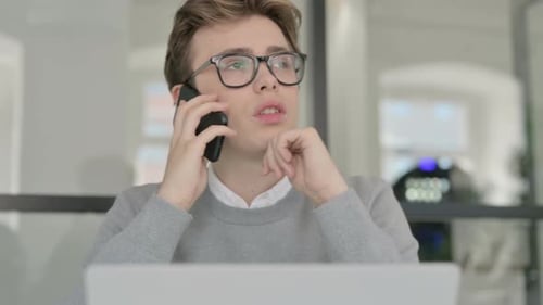 Close Up of Young Man Talking on Phone While Working on Laptop