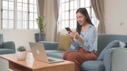Young Woman Using Mobile Phone on Sofa at Home