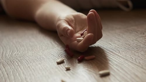 Frau liegt bewusstlos auf dem Boden mit Kapseln in der Hand