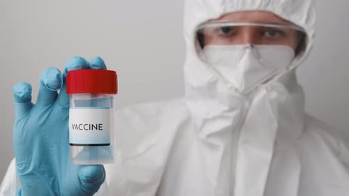 Person in Protective Suit Holding Vaccine Vial