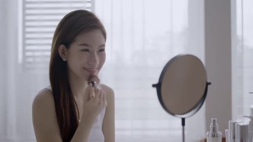 Woman Applying Makeup with Brush in Bright Room