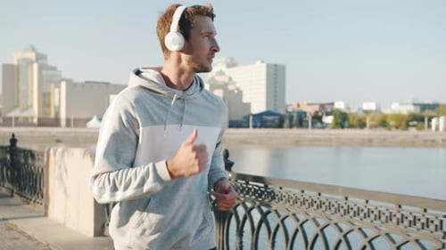 Slow Motion Portrait of Attractive Young Sportsman Jogging Outdoors Near River in Modern City