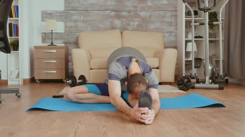 Man Does Leg Stretches on a Yoga Mat at Home