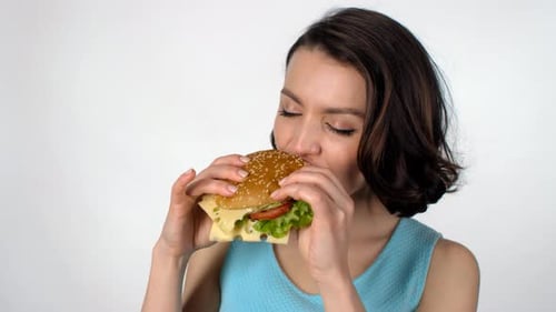 Young Woman Bites Into Large Cheeseburger Close-Up