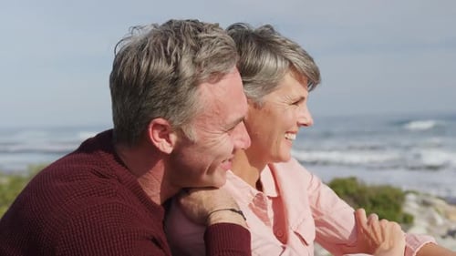 Caucasian couple enjoying free time by sea on a sunny day sitting and embracing