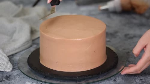 Expert Hands Smoothing Chocolate Frosting on a Cake