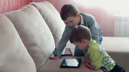 Boys Playing With Tablets On Couch Indoors