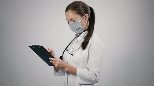 Female Doctor Writes on Clipboard Wearing Face Mask