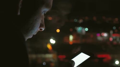 Young Man Using Smart Phone Cell App Technology at Night in Front of Blurred City Lights