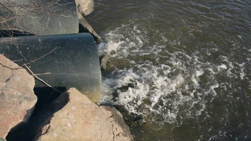 Close view of water flowing out of large sewage pipes into lake