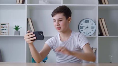 Teen Boy Video Chatting on Smartphone at Desk