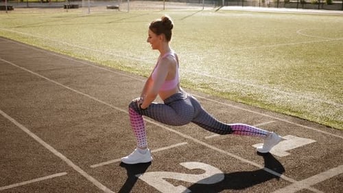 Chica joven haciendo estiramientos en el estadio en verano cuando hace sol.