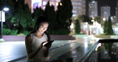 Woman using smart phone in city at night