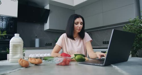 Morena sentada en la mesa de la cocina y viendo el programa culinario en línea en una