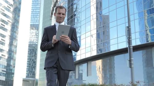 Walking Businessman Using Tablet While Walking Outside Office