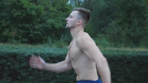 Close Up of Young Muscular Man Sprinting Fast Along Trail Near Forest at Summer Day. Handsome