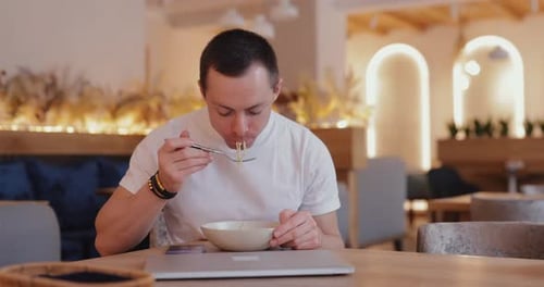 Young Adult Eats Noodles and Closes Laptop