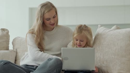 Woman and Child Look at Laptop on Couch