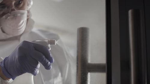 Adult in Protective Suit Disinfecting Door Handle